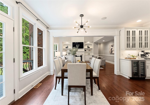 3015 Stanbury Dr, Matthews, NC 28104 - dining area featuring beverage cooler, wet bar, a chandelier, ornamental molding, and dark wood finished floors