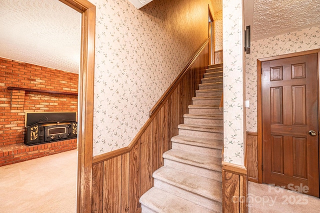 3781 Dover St, Claremont, NC 28610 - staircase with wallpapered walls, carpet floors, a textured ceiling, a wainscoted wall, and a wood stove
