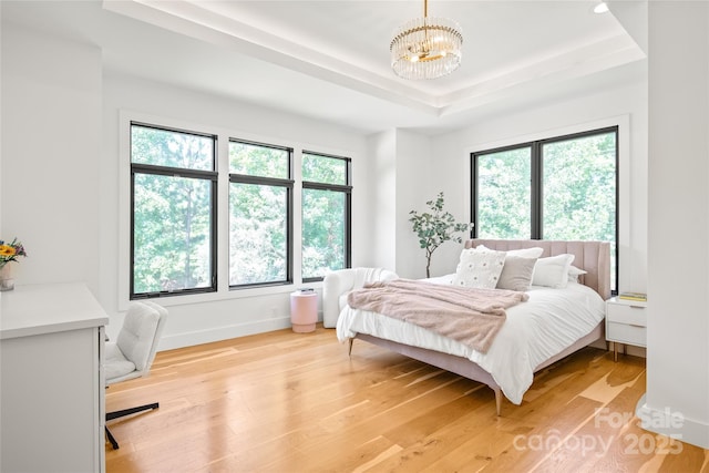 8403 Sarsfield Ct, Waxhaw, NC 28173 - bedroom featuring multiple windows, a chandelier, a tray ceiling, and light wood-style flooring