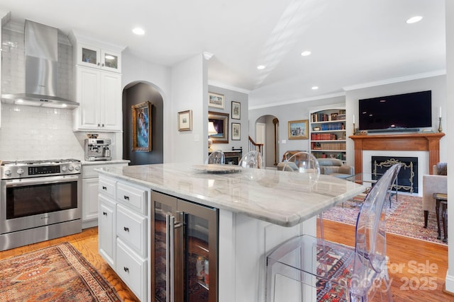 1902 4th Street Ct NW, Hickory, NC 28601 - kitchen featuring arched walkways, stainless steel gas range, beverage cooler, wall chimney range hood, and light wood finished floors