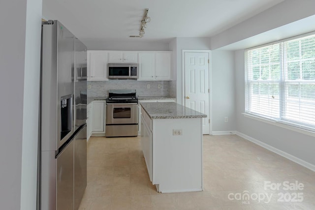 10011 Treeside Ln, Matthews, NC 28105 - kitchen with stainless steel appliances, decorative backsplash, light stone counters, a kitchen island, and white cabinetry