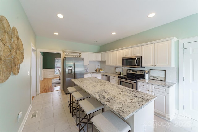 8509 Castle Cliff Dr, Matthews, NC 28105 - kitchen with appliances with stainless steel finishes, a kitchen island, a breakfast bar area, light stone countertops, and white cabinetry