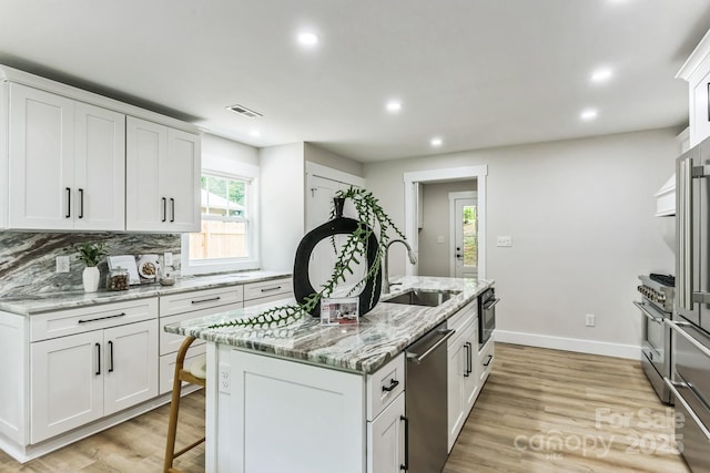 1208 Tarrington Ave, Charlotte, NC 28205 - kitchen with appliances with stainless steel finishes, recessed lighting, white cabinetry, an island with sink, and light wood finished floors