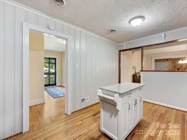 209 11th St, Spencer, NC 28159 - kitchen featuring crown molding, light wood-style flooring, white cabinetry, a textured ceiling, and light stone counters