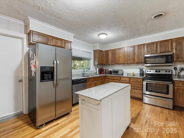 209 11th St, Spencer, NC 28159 - kitchen with stainless steel appliances, crown molding, light wood finished floors, a textured ceiling, and a kitchen island