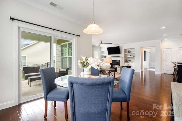 3021 Henshaw Rd, Waxhaw, NC 28173 - dining space featuring built in shelves, crown molding, dark wood-type flooring, a warm lit fireplace, and a ceiling fan
