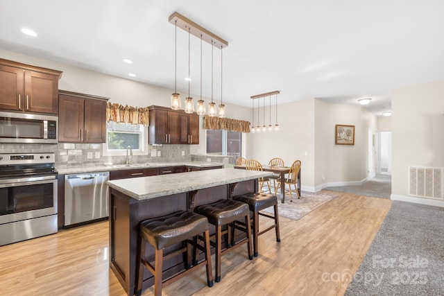 240 Red Cedar Rd, Mooresville, NC 28115 - kitchen featuring stainless steel appliances, decorative backsplash, a kitchen bar, light wood-style flooring, and a center island