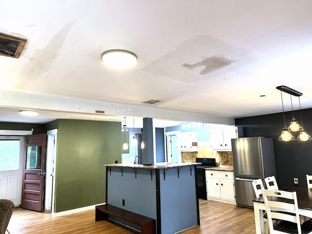 491 W Main St, Waldoboro, ME 04572 - kitchen with freestanding refrigerator, gas stove, a breakfast bar area, white cabinetry, and light wood finished floors