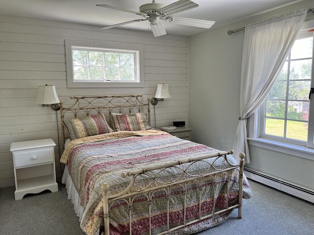 carpeted bedroom with multiple windows, ceiling fan, baseboard heating, and wood walls