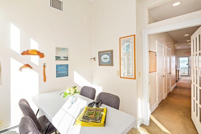 dining space featuring baseboard heating, light colored carpet, and a high ceiling