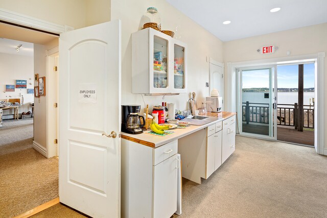 kitchen featuring a water view, light colored carpet, white cabinets, and sink