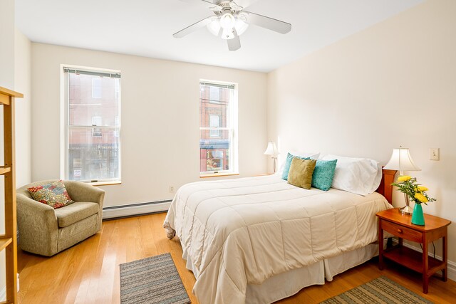 bedroom with light hardwood / wood-style flooring, ceiling fan, and a baseboard heating unit