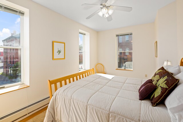 bedroom with multiple windows, light hardwood / wood-style floors, and a baseboard heating unit