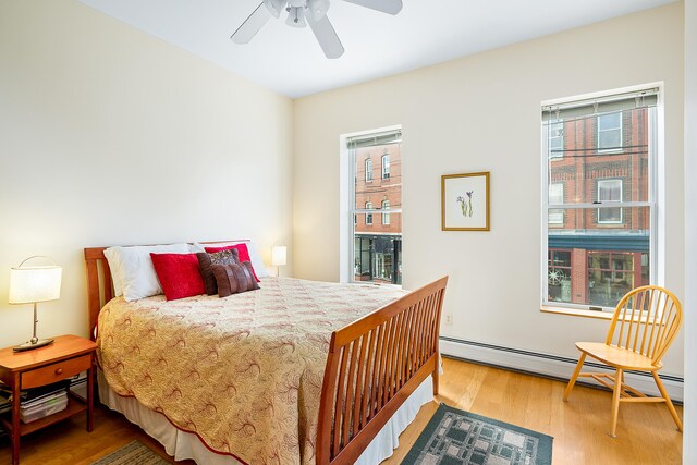 bedroom with ceiling fan, multiple windows, light wood-type flooring, and a baseboard heating unit