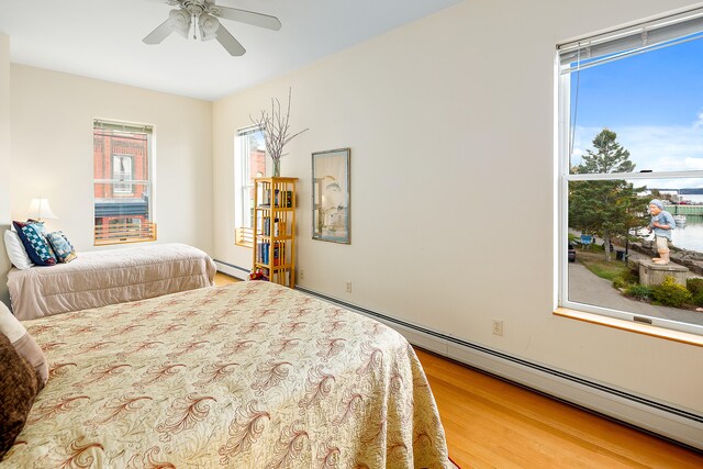 bedroom featuring baseboard heating, multiple windows, ceiling fan, and light wood-type flooring