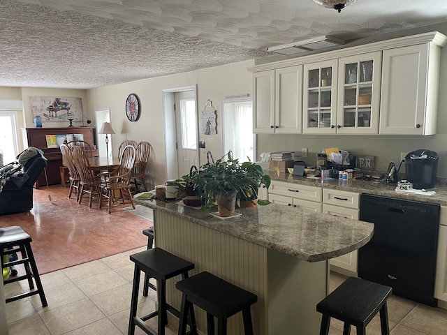 kitchen featuring light stone counters, a kitchen breakfast bar, black dishwasher, a textured ceiling, and white cabinetry