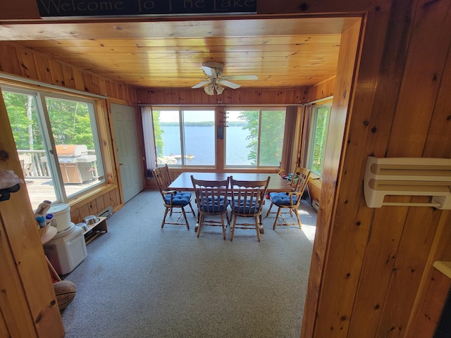 dining space with wood walls, a water view, wood ceiling, ceiling fan, and carpet