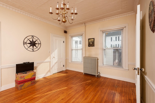 empty room featuring radiator heating unit, ornamental molding, an inviting chandelier, and dark wood-type flooring