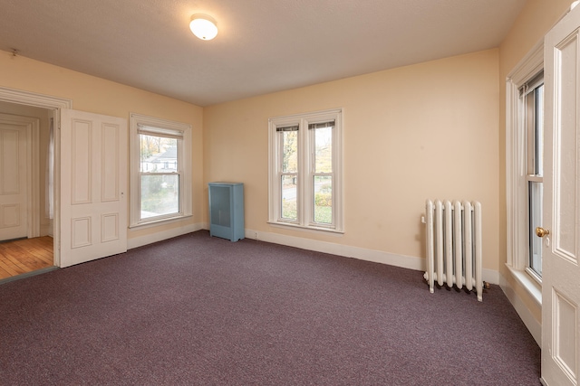 spare room featuring dark carpet and radiator