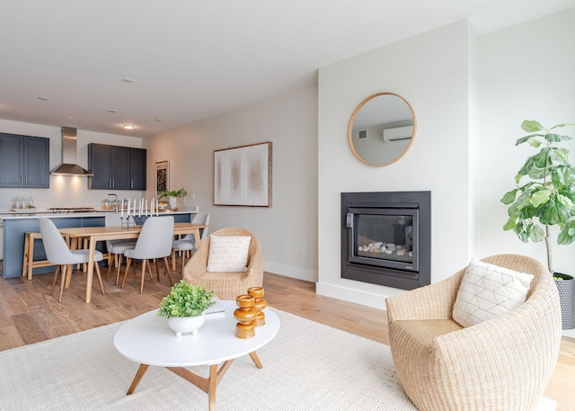 living room featuring baseboards, light wood-style flooring, a glass covered fireplace, and a wall mounted air conditioner