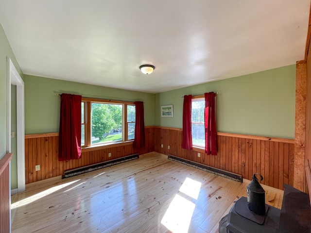 empty room with baseboard heating, a healthy amount of sunlight, and light hardwood / wood-style floors