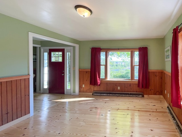 entrance foyer with a baseboard heating unit, wood walls, and light wood-type flooring