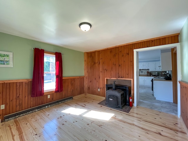 unfurnished living room with wooden walls, a wood stove, and light hardwood / wood-style floors