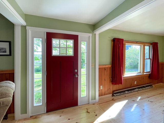 foyer featuring light wood-type flooring, a healthy amount of sunlight, and wooden walls