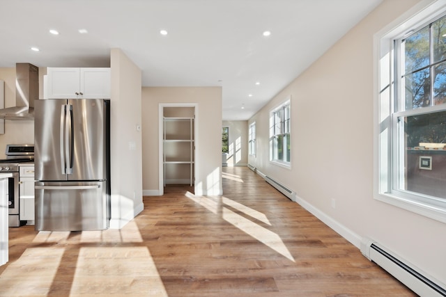 kitchen featuring light wood-style floors, appliances with stainless steel finishes, a baseboard radiator, and wall chimney exhaust hood