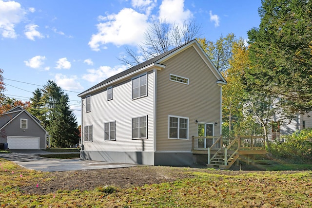 rear view of property featuring a detached garage and a wooden deck