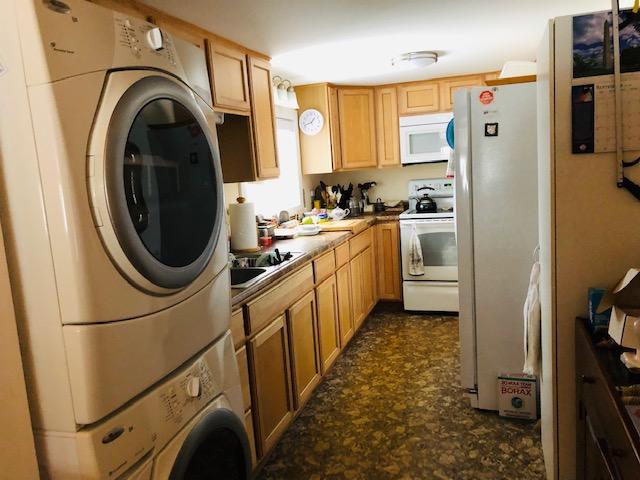 kitchen featuring sink, white appliances, stacked washer and dryer, and dark tile floors