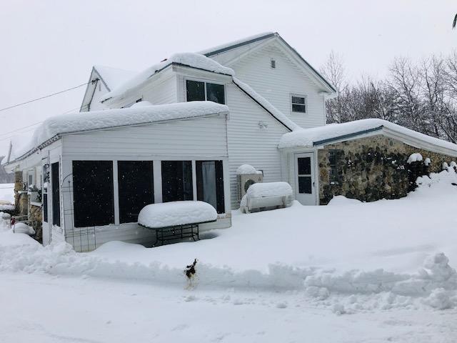 snow covered back of property featuring a sunroom