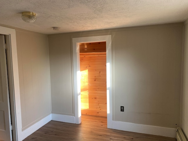 unfurnished room with a textured ceiling, dark hardwood / wood-style floors, and a baseboard heating unit