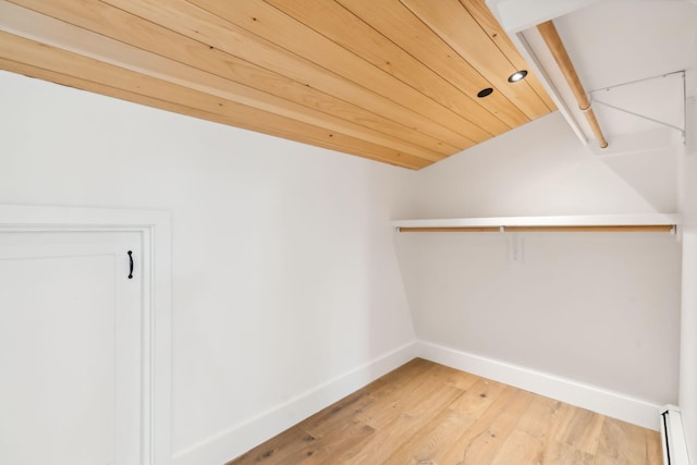 spacious closet with a baseboard radiator, wood-type flooring, and vaulted ceiling with beams