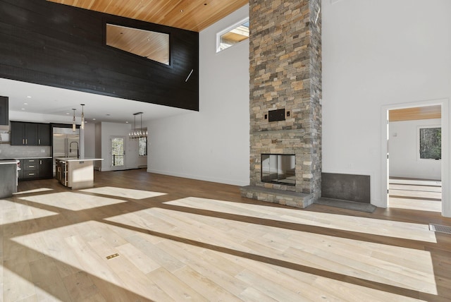 unfurnished living room featuring a stone fireplace, a high ceiling, hardwood / wood-style flooring, wood ceiling, and an inviting chandelier