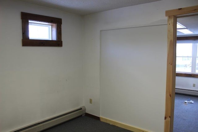 empty room with a baseboard radiator, a textured ceiling, and dark carpet