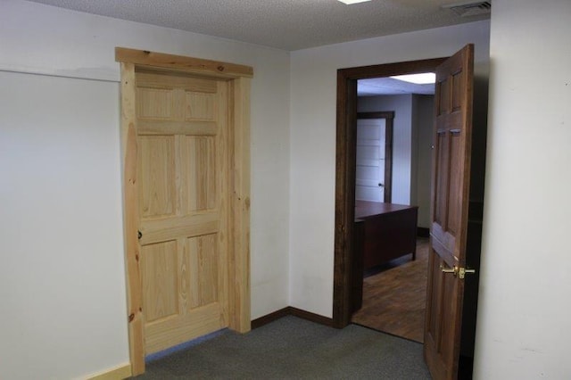 hallway with a textured ceiling and dark colored carpet