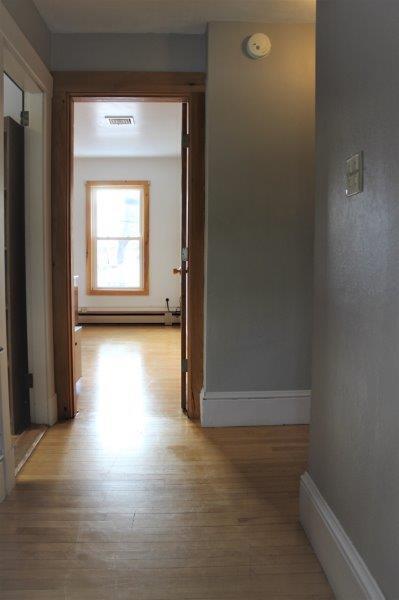 hall with baseboard heating and light wood-type flooring