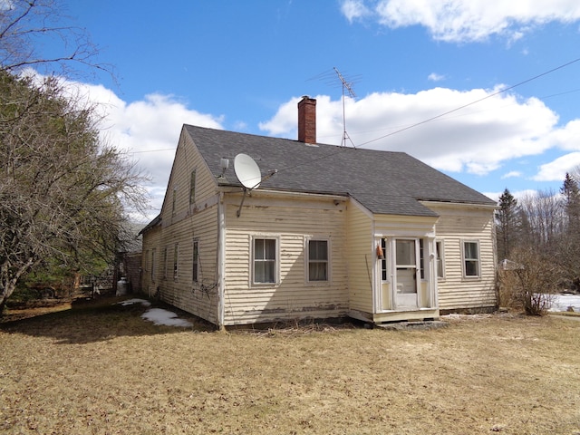 rear view of house featuring a chimney, a yard, and a shingled roof