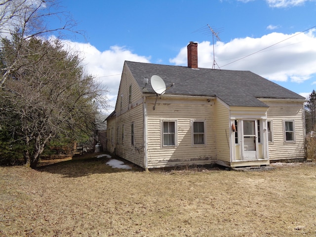 back of house with a chimney, a yard, and roof with shingles