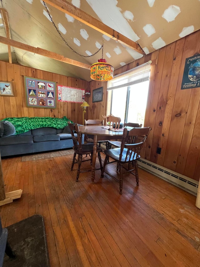 dining room featuring lofted ceiling with beams, a baseboard heating unit, wooden walls, and hardwood / wood-style floors