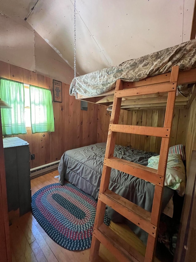 bedroom with lofted ceiling, hardwood / wood-style flooring, wooden walls, and a baseboard radiator