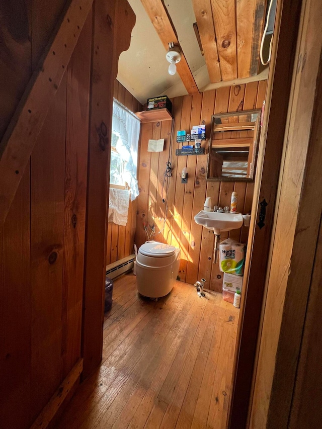 bathroom featuring toilet, wood-type flooring, sink, lofted ceiling with beams, and wood walls