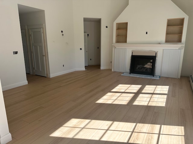 unfurnished living room with built in features, high vaulted ceiling, and light wood-type flooring