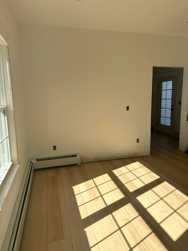 unfurnished room featuring a baseboard heating unit and light hardwood / wood-style floors