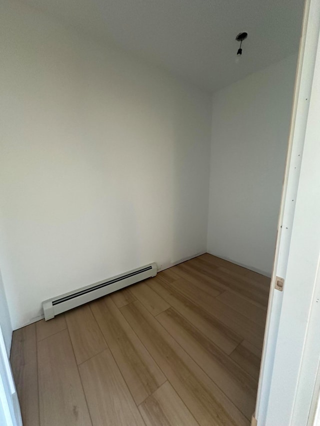 unfurnished room featuring wood-type flooring and a baseboard heating unit