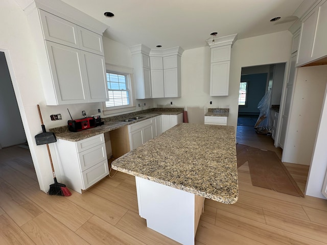 kitchen featuring light wood-type flooring, a center island, white cabinets, light stone counters, and a breakfast bar area