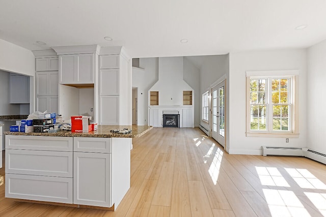 kitchen featuring a kitchen island, french doors, a baseboard heating unit, dark stone countertops, and light hardwood / wood-style floors