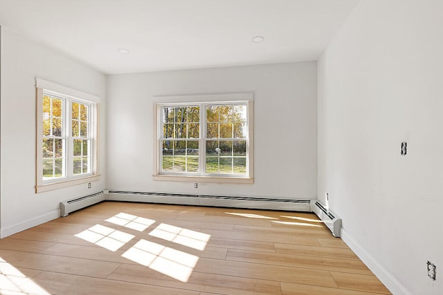 unfurnished room with a baseboard heating unit, a healthy amount of sunlight, and light wood-type flooring