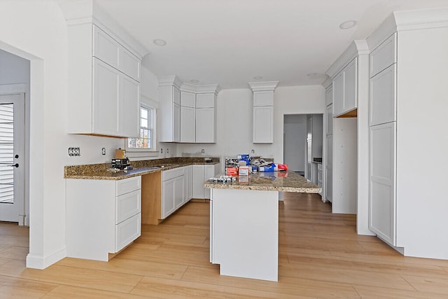 kitchen with white cabinets, a kitchen island, a kitchen bar, light hardwood / wood-style flooring, and dark stone countertops